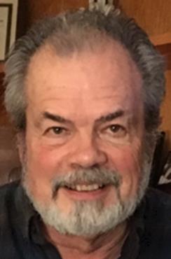 A man with grey hair and beard smiling for the camera.